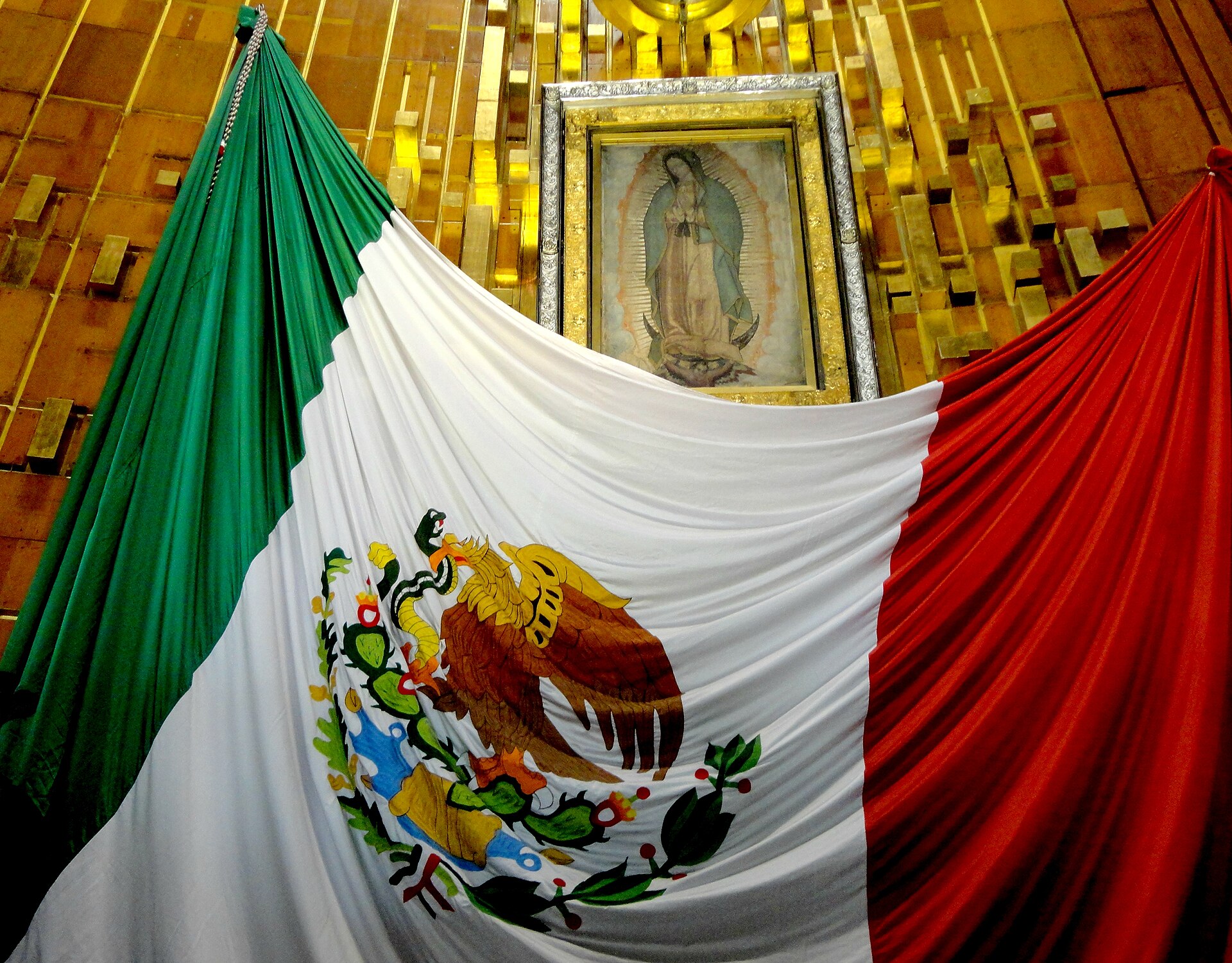 Tấm tilma gốc được treo trong Vương cung thánh đường Guadalupe tại Mexico City, phía trước là quốc kỳ Mexico